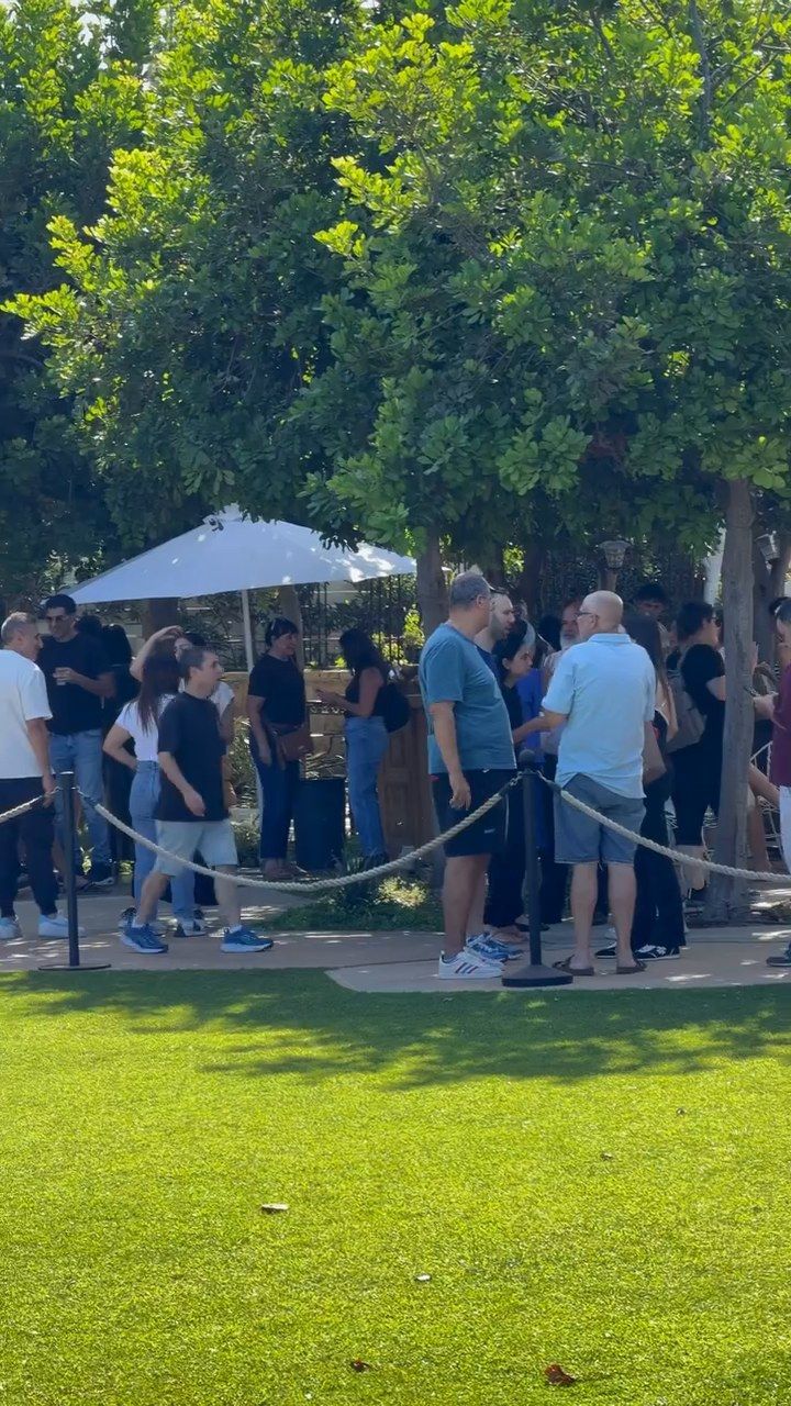 אורחים עומדים בתור על הדשא, ליד שמשייה לבנה, באירוע חברה